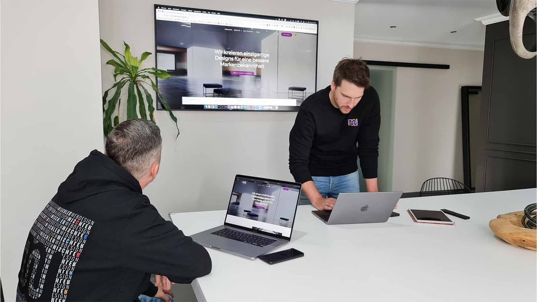 Team von Mischler Webdesign bei einer Projektbesprechung mit Laptops und Website-Entwurf auf dem Wandbildschirm