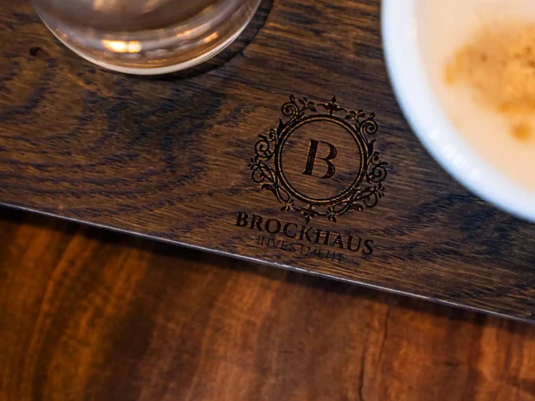 Holzbrett mit eingraviertem Brockhaus-Logo neben Getränken: Titelbild der Referenz Brockhaus Immobilien