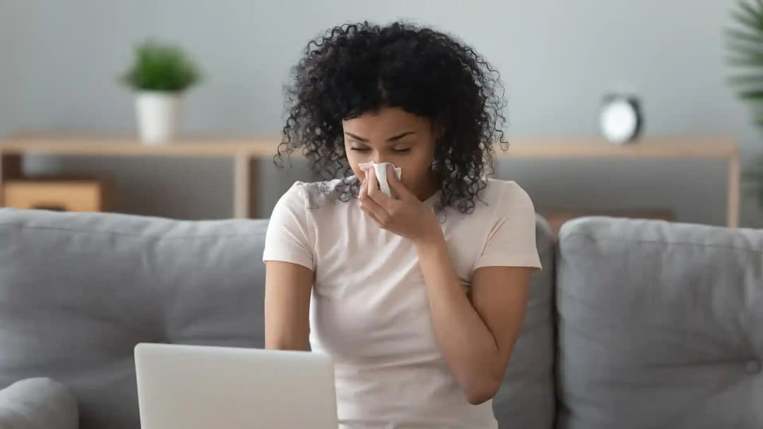Frau mit Taschentuch niest auf dem Sofa: Titelbild der Referenz Conveclean zur Heizkörperreinigung für Privatkunden